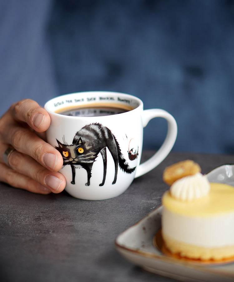 Tasse mit Katze steht auf einem Tisch im Café neben einem Törtchen